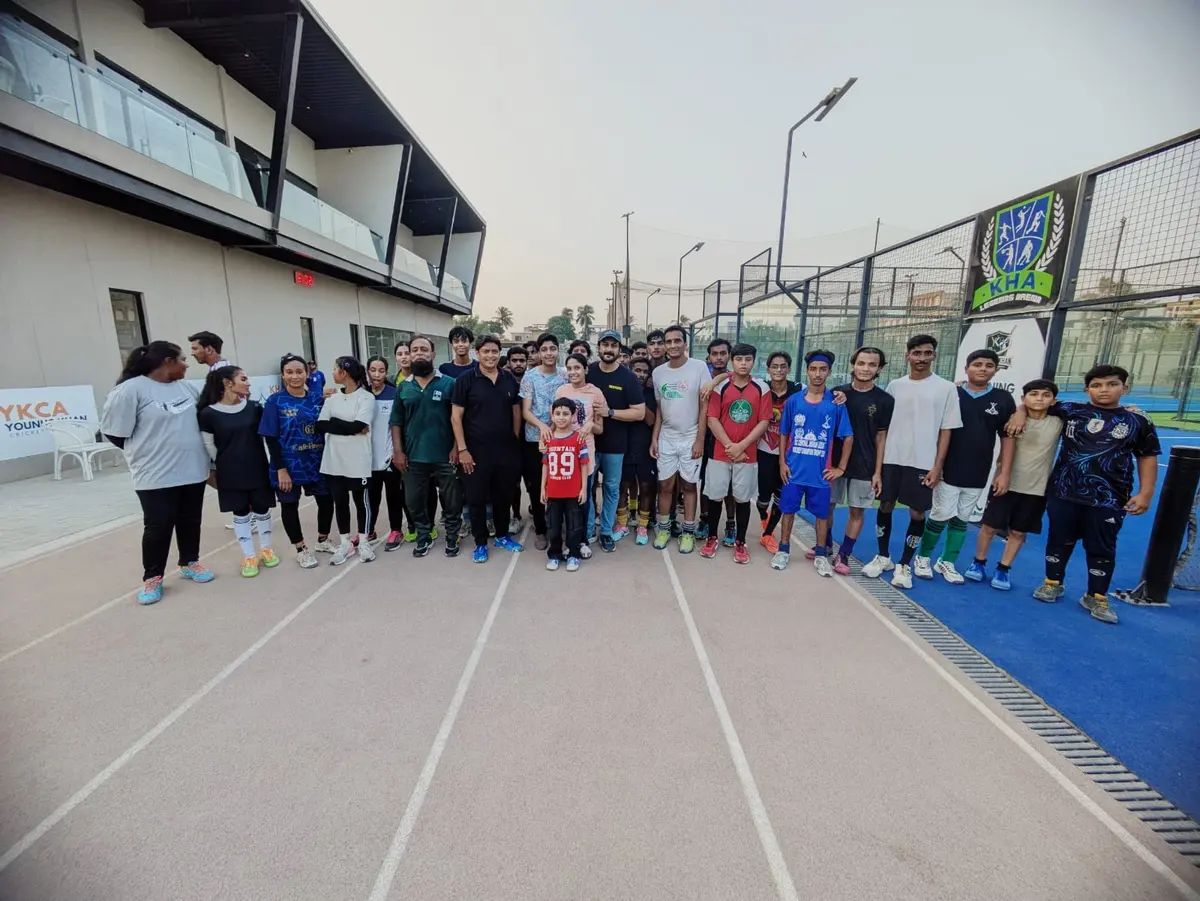 Kamran Jilani standing with dozens of boys and girls from KHA's training group on the running track beside the blue pitch